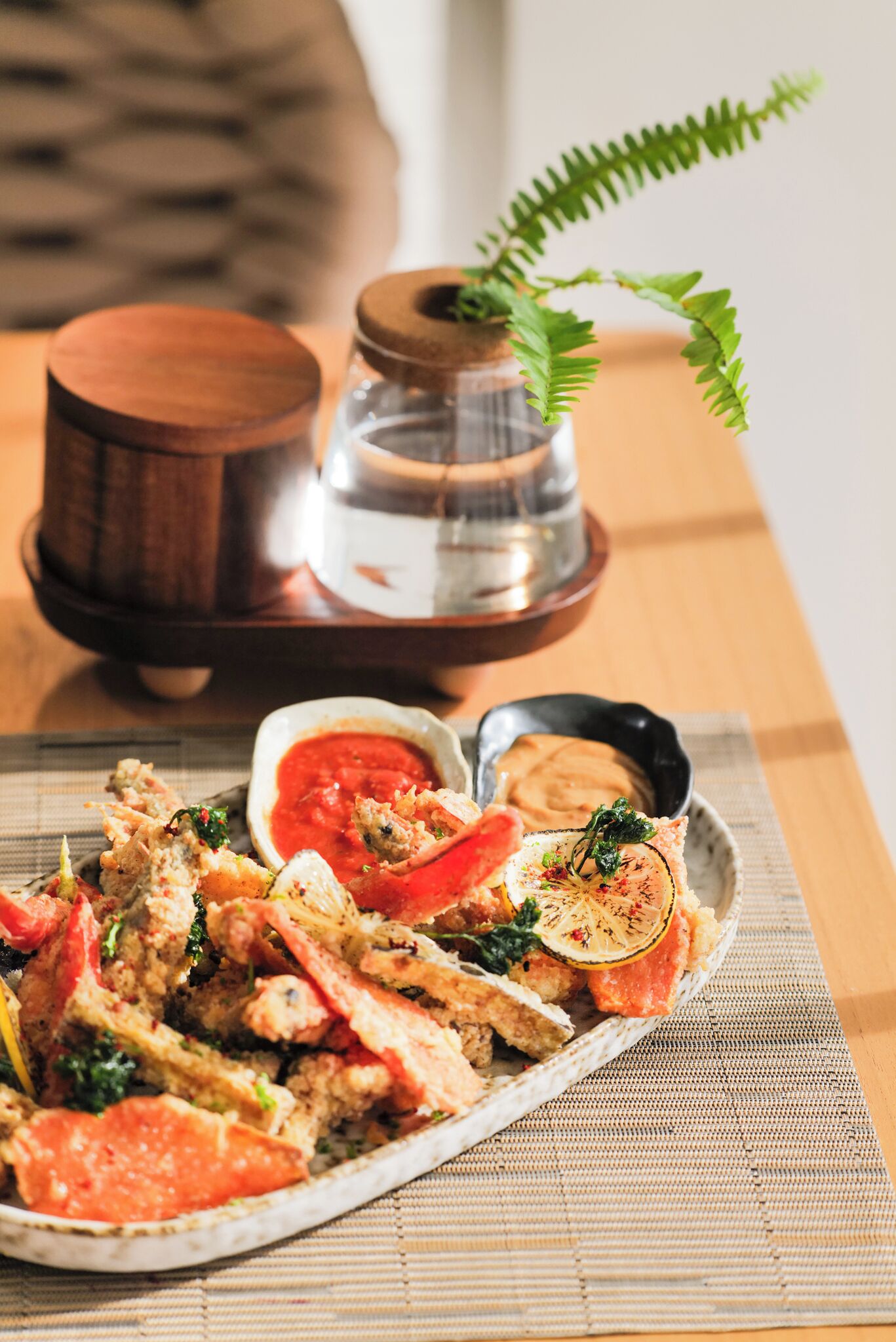 Een bord eten met verschillende ingrediënten, zoals een plak tomaat en bladgroenten, vergezeld van een klein bakje saus en een zwarte kom met saus.