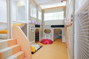 Zona de juegos infantiles con estructura de juegos suaves, un tobogán y una pared de escalada.