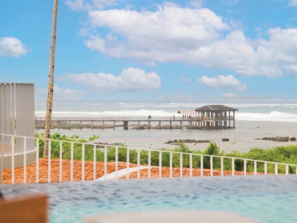 Blick auf einen Strand mit einer Mole, einem Pool und einem weißen Gebäude.