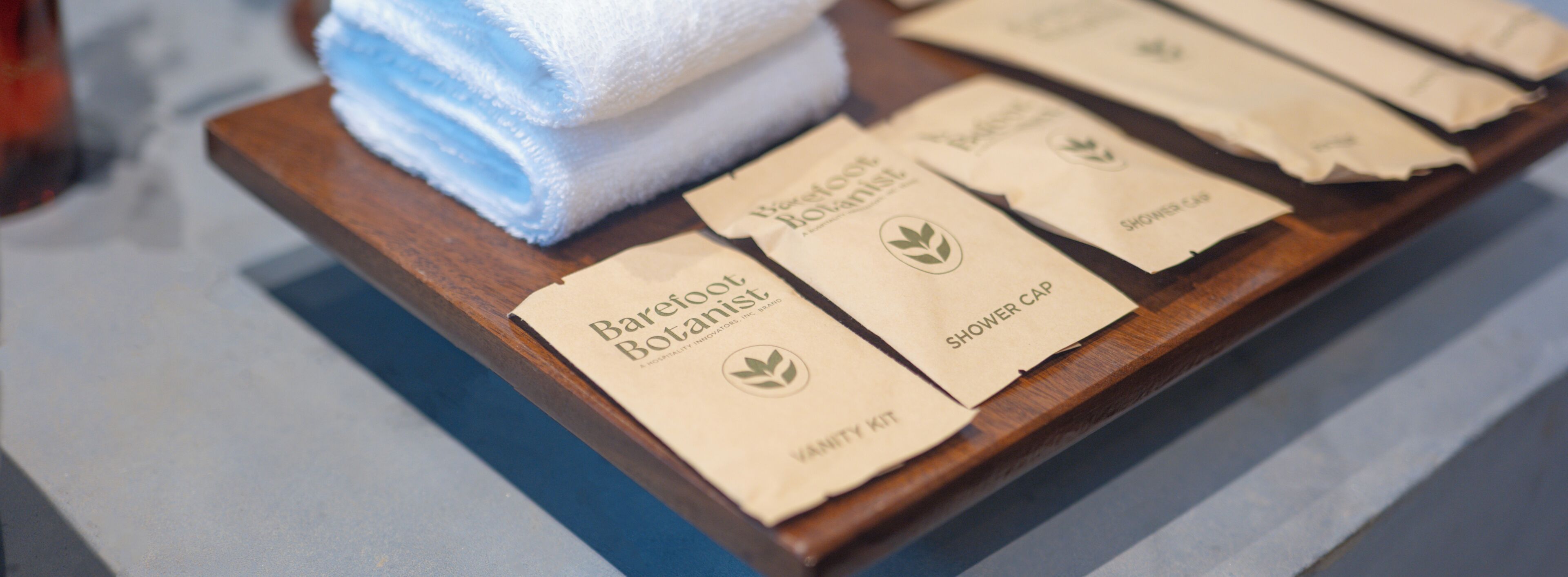 A wooden tray with a folded towel and several packaged items labeled 'Barefoot Botanist.'