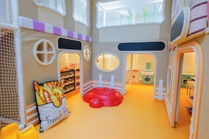 Ein Kinderspielbereich mit einer roten Schildkröten-Spielkonstruktion, einem weißen Zaun und einem Spielhäuschen mit Fenstern.