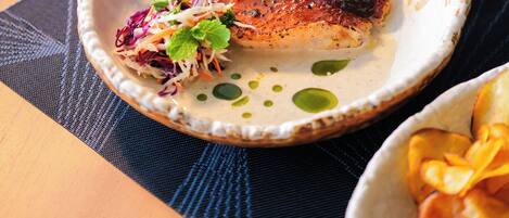 A plate of food with a fish, greens, and a side salad on a textured placemat.