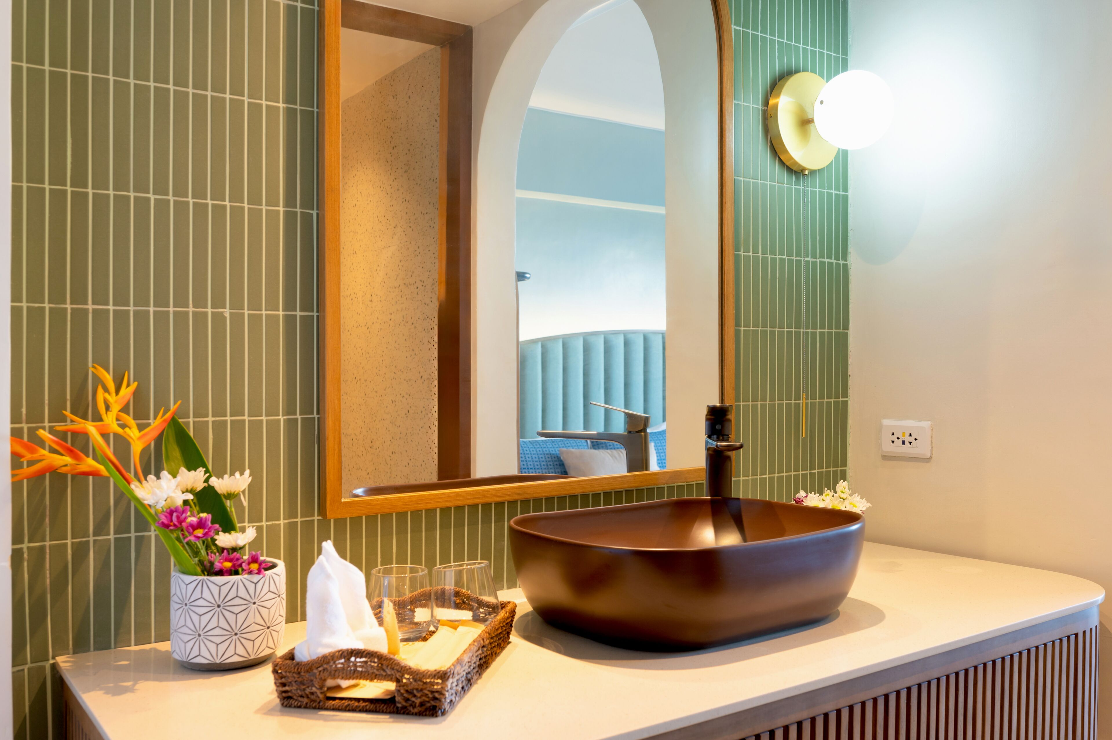 A bathroom with a large vessel sink, a mirror, a vase with flowers, and a towel rack.