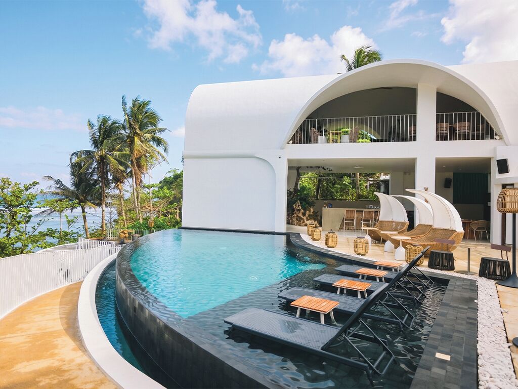 Un moderno resort con piscina, sillones de descanso y un edificio de dos plantas.