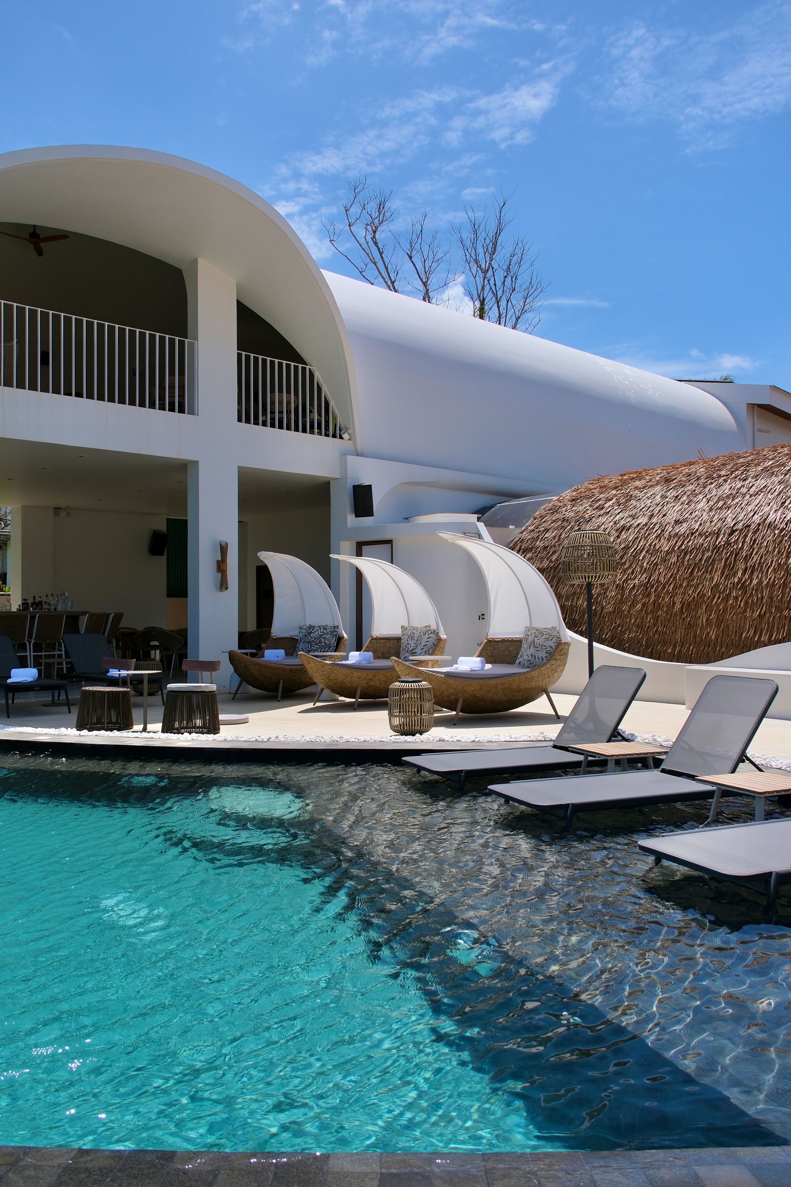 A poolside area with lounge chairs, a bar, and a thatched structure.