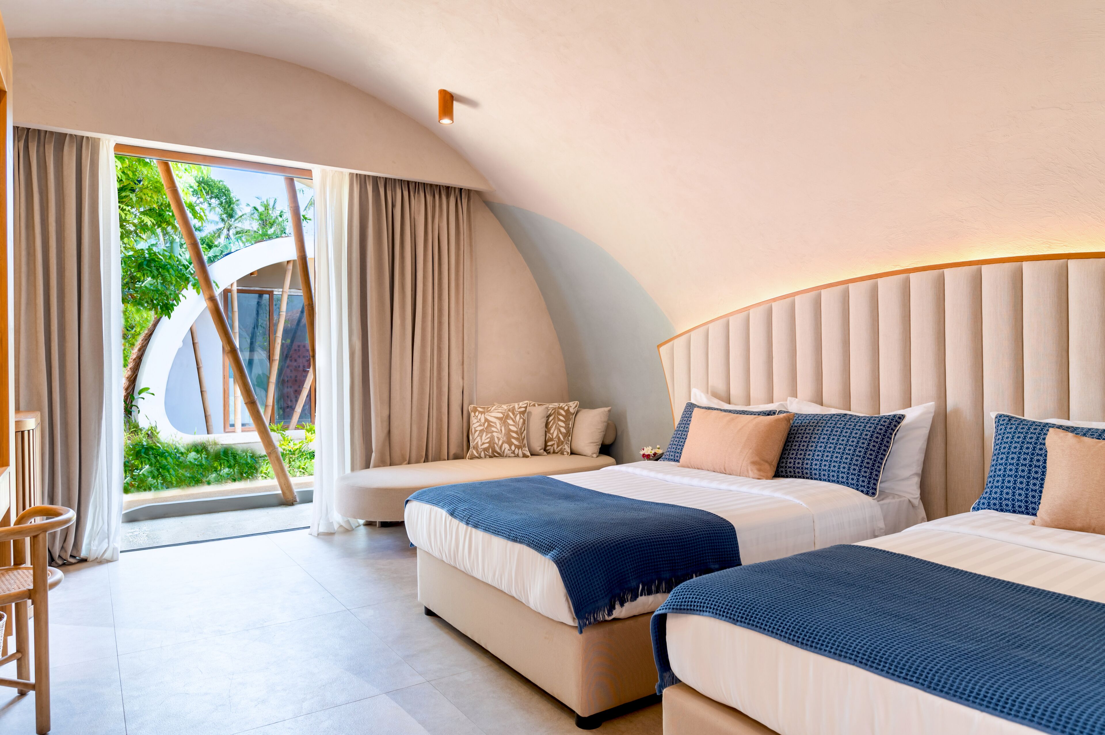 A hotel room with two beds, a curved ceiling, and a view of greenery outside.
