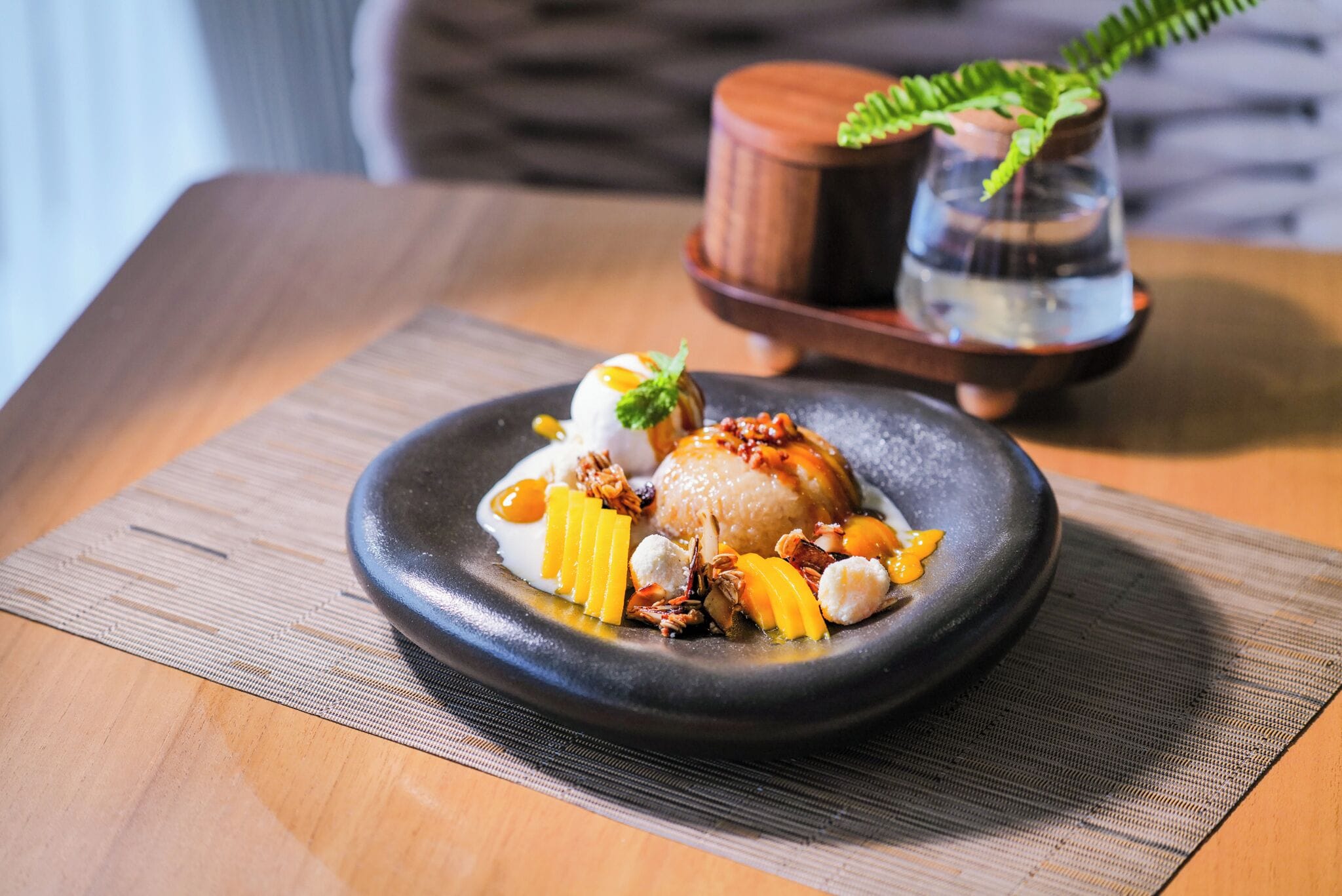 A dessert on a black plate with a wooden table and a small potted plant in the background.