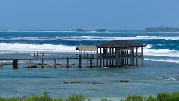 En brygga som sträcker sig ut i havet, med en byggnad i änden, omgiven av grönska.