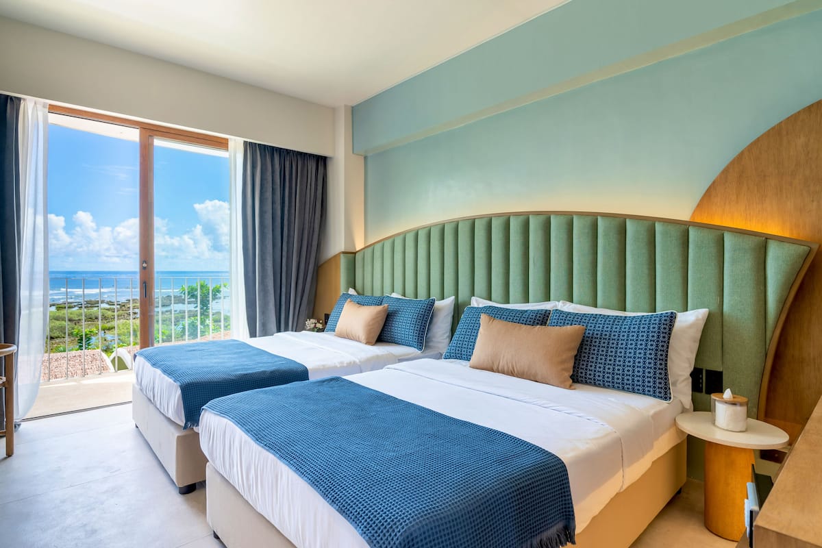 Habitació d'hotel amb dos llits, vista a l'oceà i un balcó.