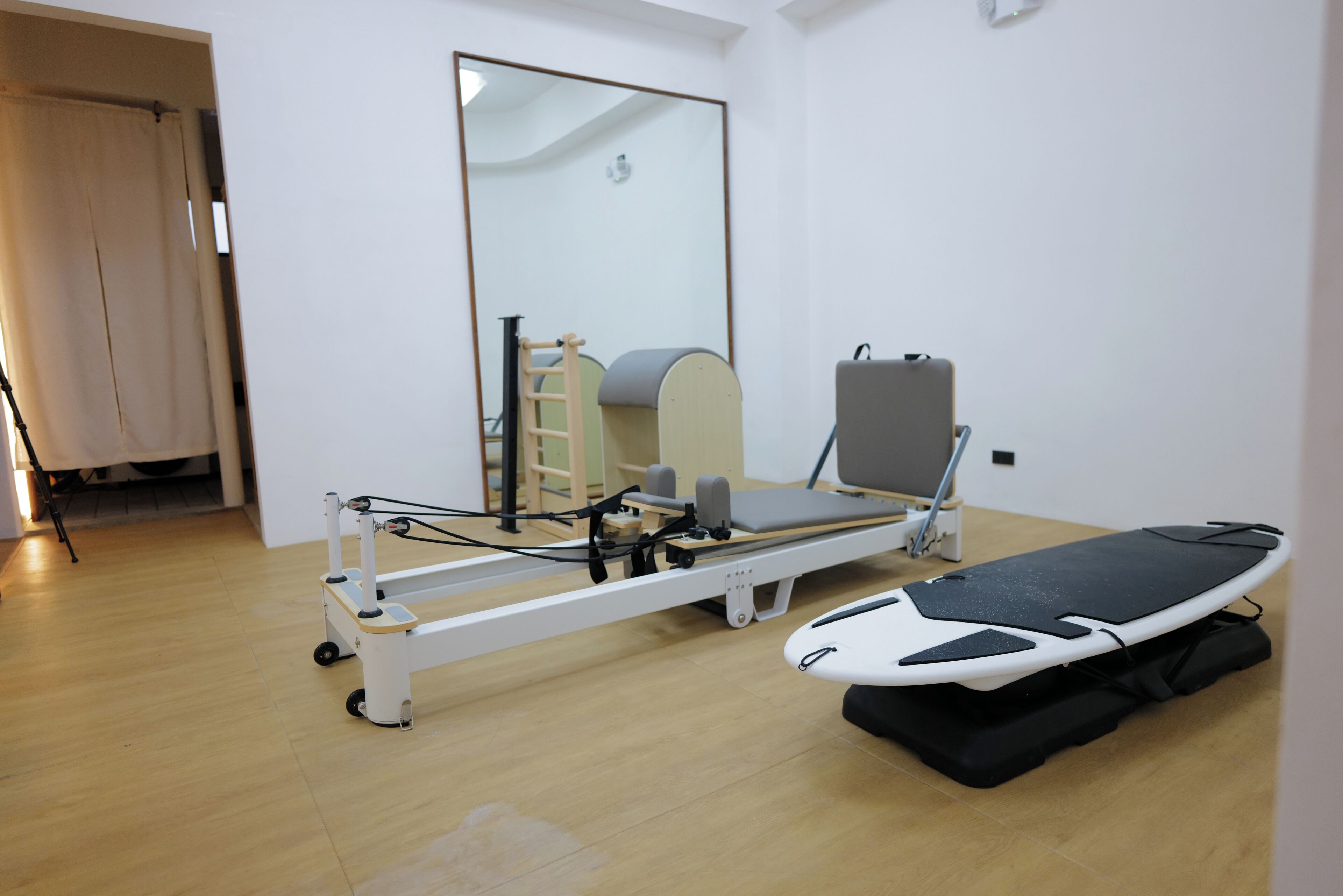 A medical examination room with a treatment table, a mirror, and a wooden floor.