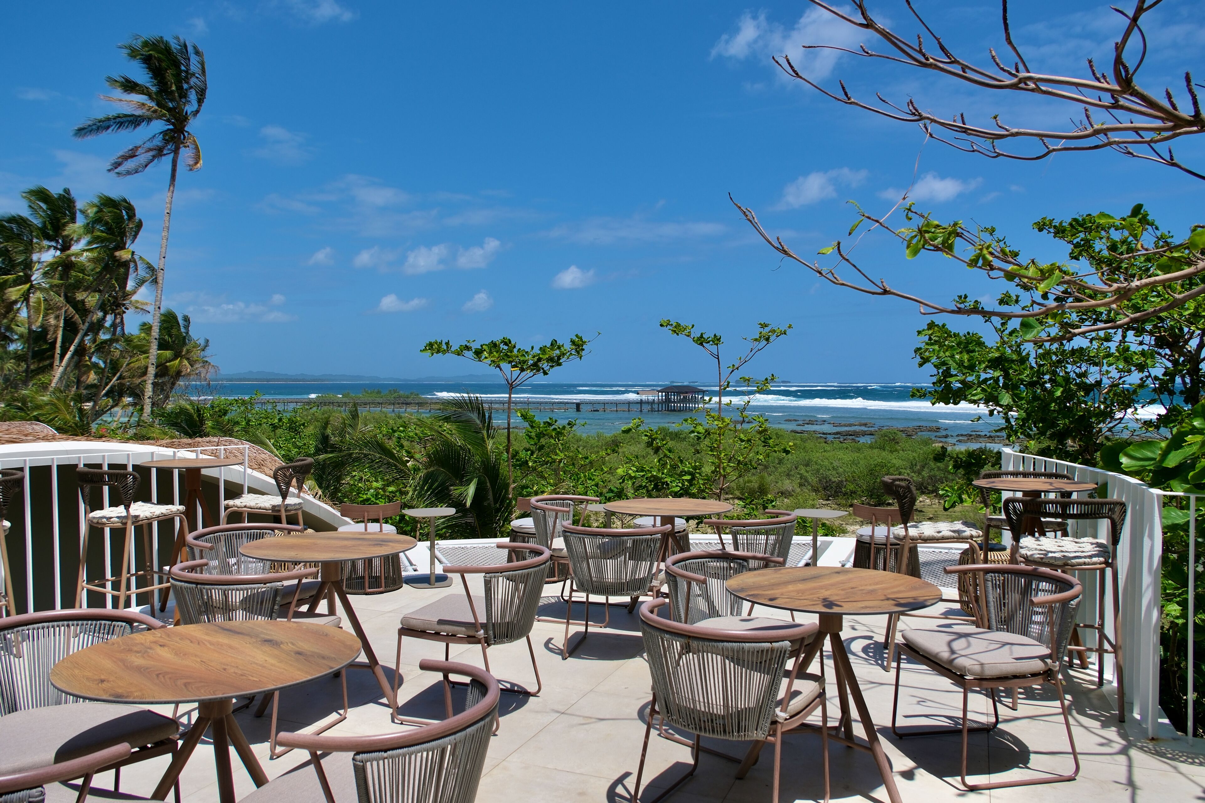 A terrace with outdoor seating, overlooking a beach and ocean.