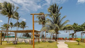 A beachside resort with a wooden pergola, lounge chairs, and a pathway leading to the beach.