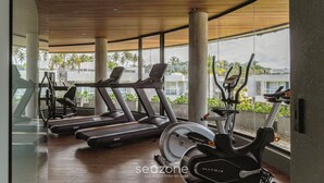 A gym with treadmills, elliptical machines, and a rowing machine, featuring large windows and a wooden ceiling.