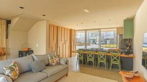 A modern living room with a grey sofa, wooden panel wall, and a kitchen area with bar stools.
