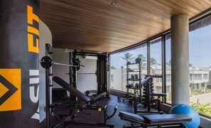 A gym with weightlifting equipment, a bench, and a large window offering a view of palm trees and buildings.