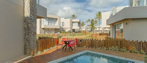 A modern pool area with a wooden deck, stone walls, and a red table with chairs.