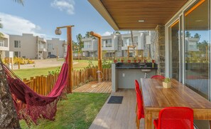 A modern outdoor patio with a wooden table and red chairs, a hammock, and a stone wall. - House With Pool at Praia do Marceneiro Nluh0008 (Passo de Camaragibe)
