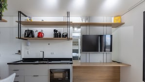 Una cocina moderna con horno empotrado, microondas y un televisor de pantalla plana grande. Hay repisas de madera sobre la encimera y una ventana pequeña sobre el televisor.