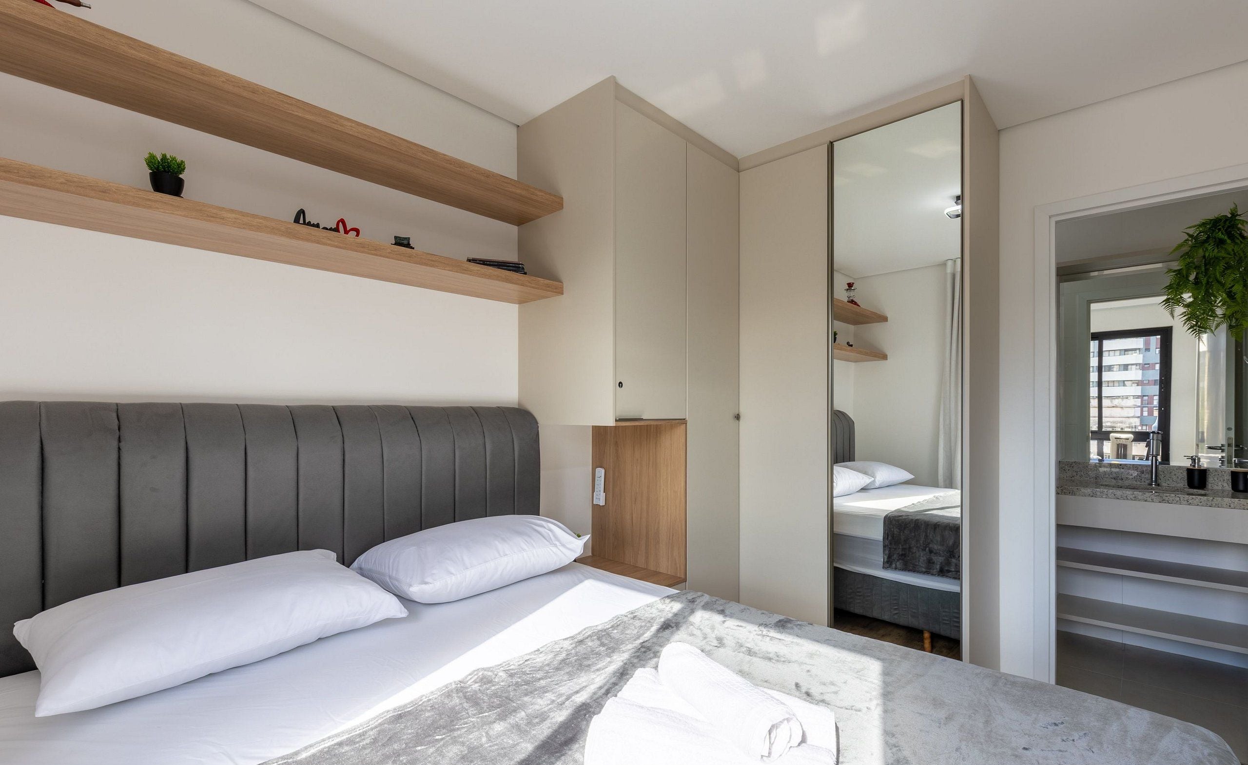 A modern bedroom with a bed, built-in shelves, a wardrobe, and a mirror.