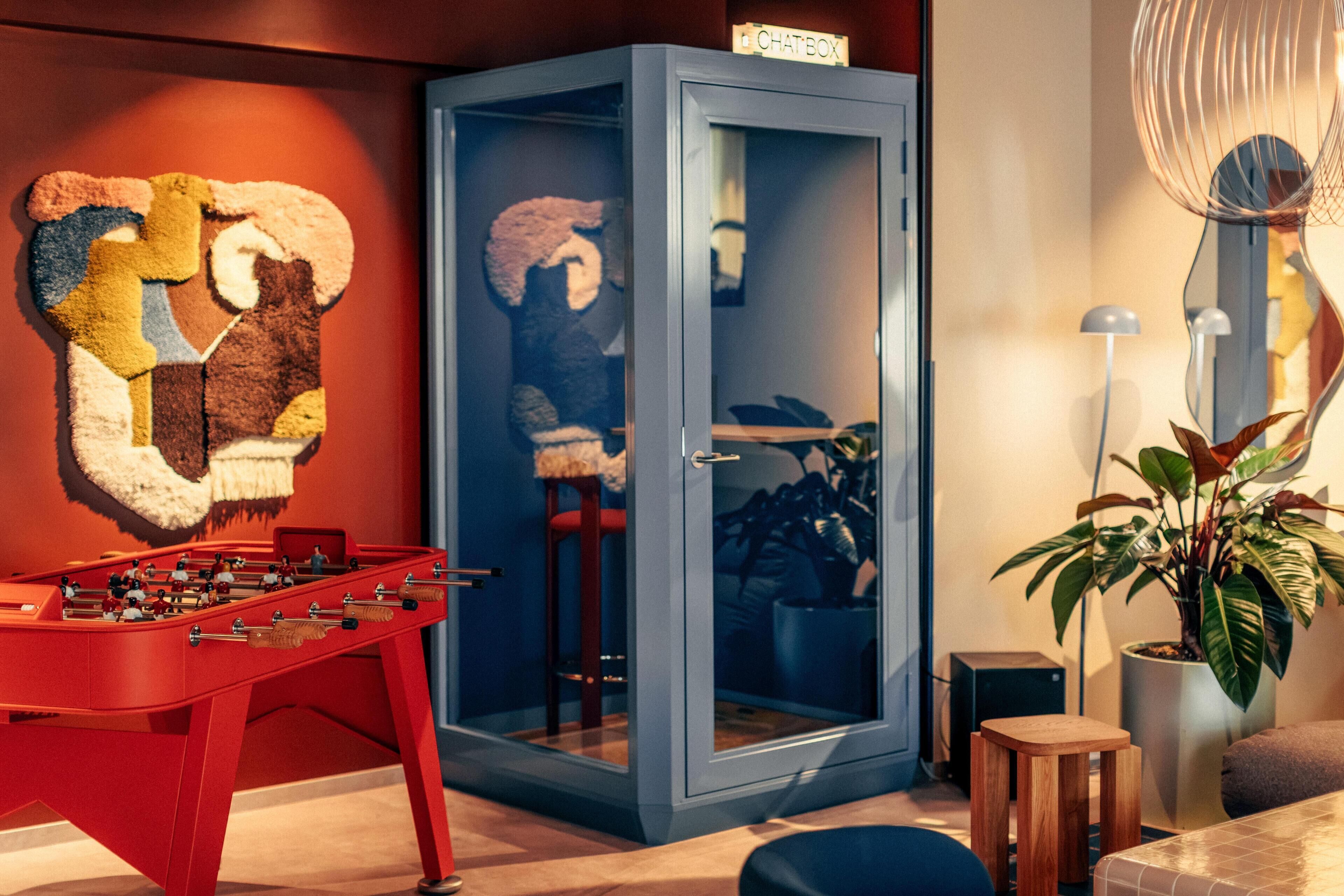 A room with a foosball table, a glass cabinet with a teddy bear, a plant, and a lamp.