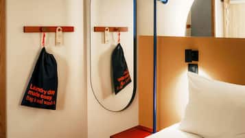 A hotel room with a bed, a nightstand, a mirror, and a wall-mounted towel rack with a black towel and a tag.
