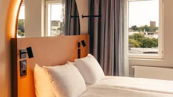 A hotel room with a bed, a window with curtains, and a view of buildings.