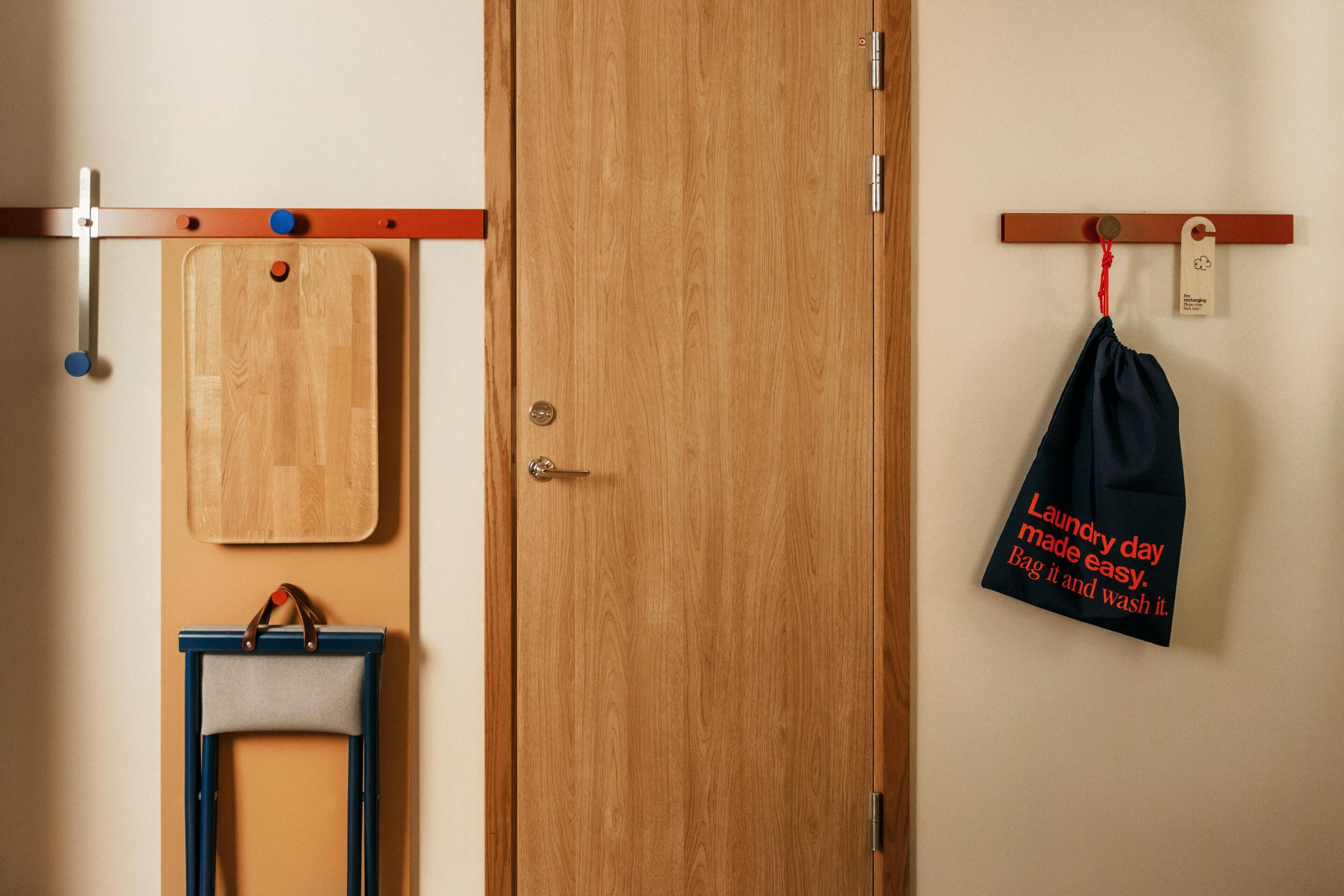 Un armario de madera con una puerta, una silla azul y una tabla de cortar de madera colgada en la pared.