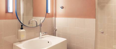 Une salle de bain avec un lavabo blanc, un miroir et une douche.