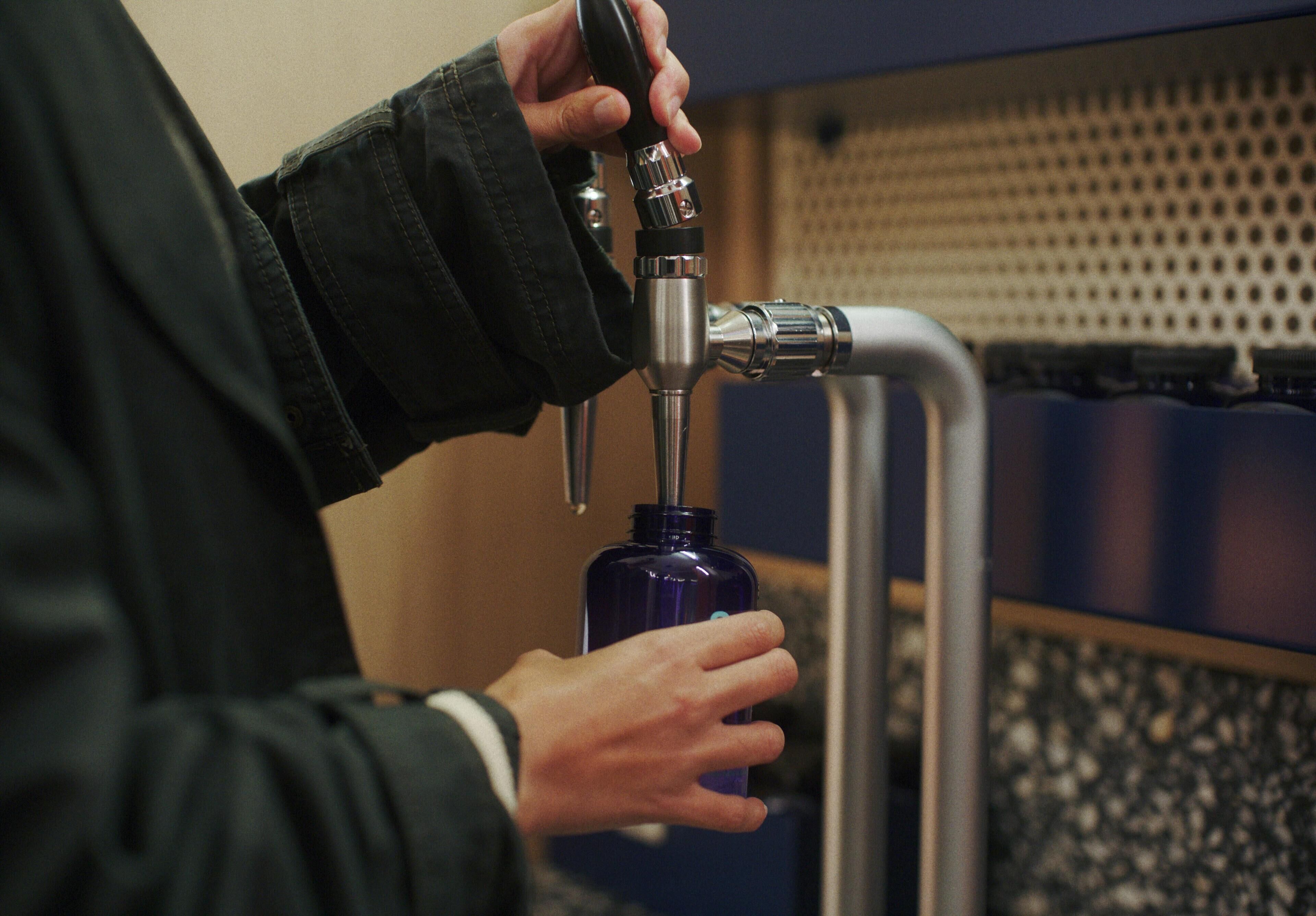 A person using a water tap to fill a bottle.
