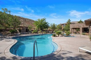 A swimming pool with a curved edge, surrounded by a patio area with lounge chairs and a mountain backdrop.