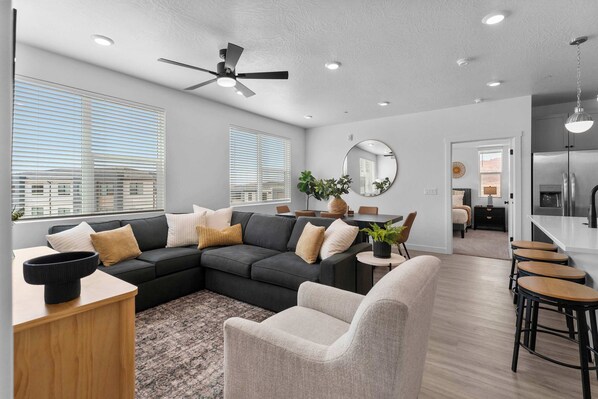 A modern living room with a sectional sofa, a dining area, and a kitchen.