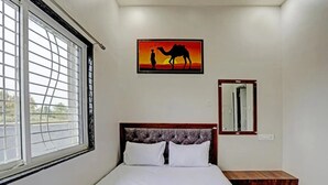 Ein Schlafzimmer mit einem Bett, einem Nachttisch, einem Fenster mit Ausblick, einem Gemälde mit einem Kamel und einer Person sowie einem Spiegel.