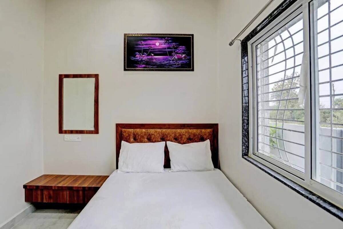 Een slaapkamer met een bed, een raam, een aan de muur hangend schilderij en een klein houten tafeltje.