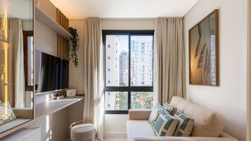 Una sala de estar moderna con un sofá, un televisor, una mesita y un ventanal con vista a la ciudad.