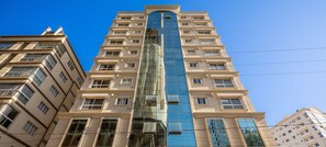 Un edificio a grattacielo con una facciata centrale in vetro, numerosi balconi e un design architettonico moderno.