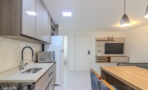 Cozinha moderna com micro-ondas, fogão e pia embutidos. Há uma área de refeições com mesa e cadeiras de madeira.