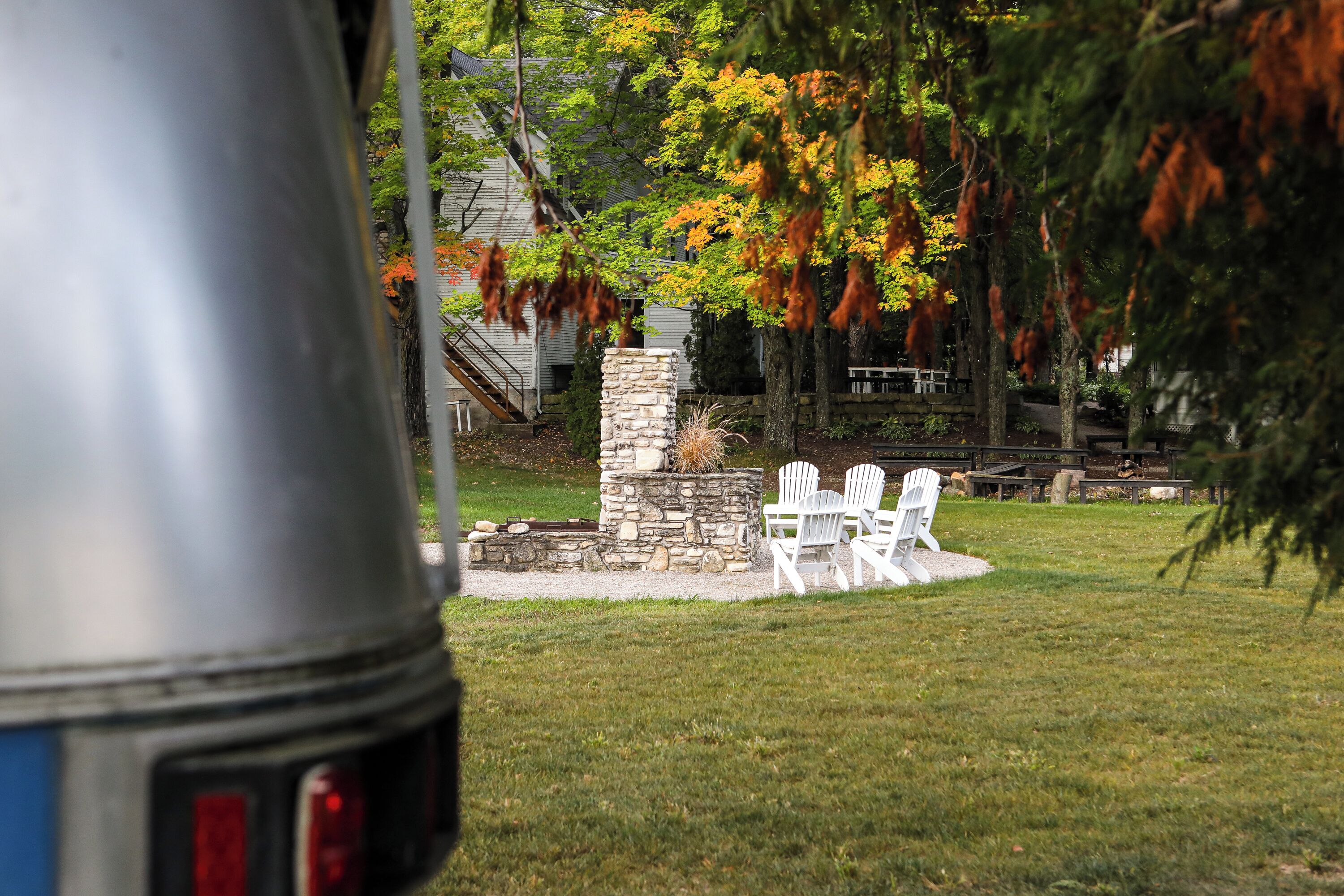 A stone structure with a fire pit and white chairs in a grassy area.