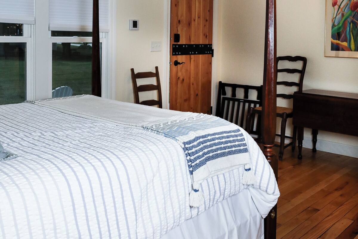 A bedroom with a bed, wooden floor, a door, and a chair.