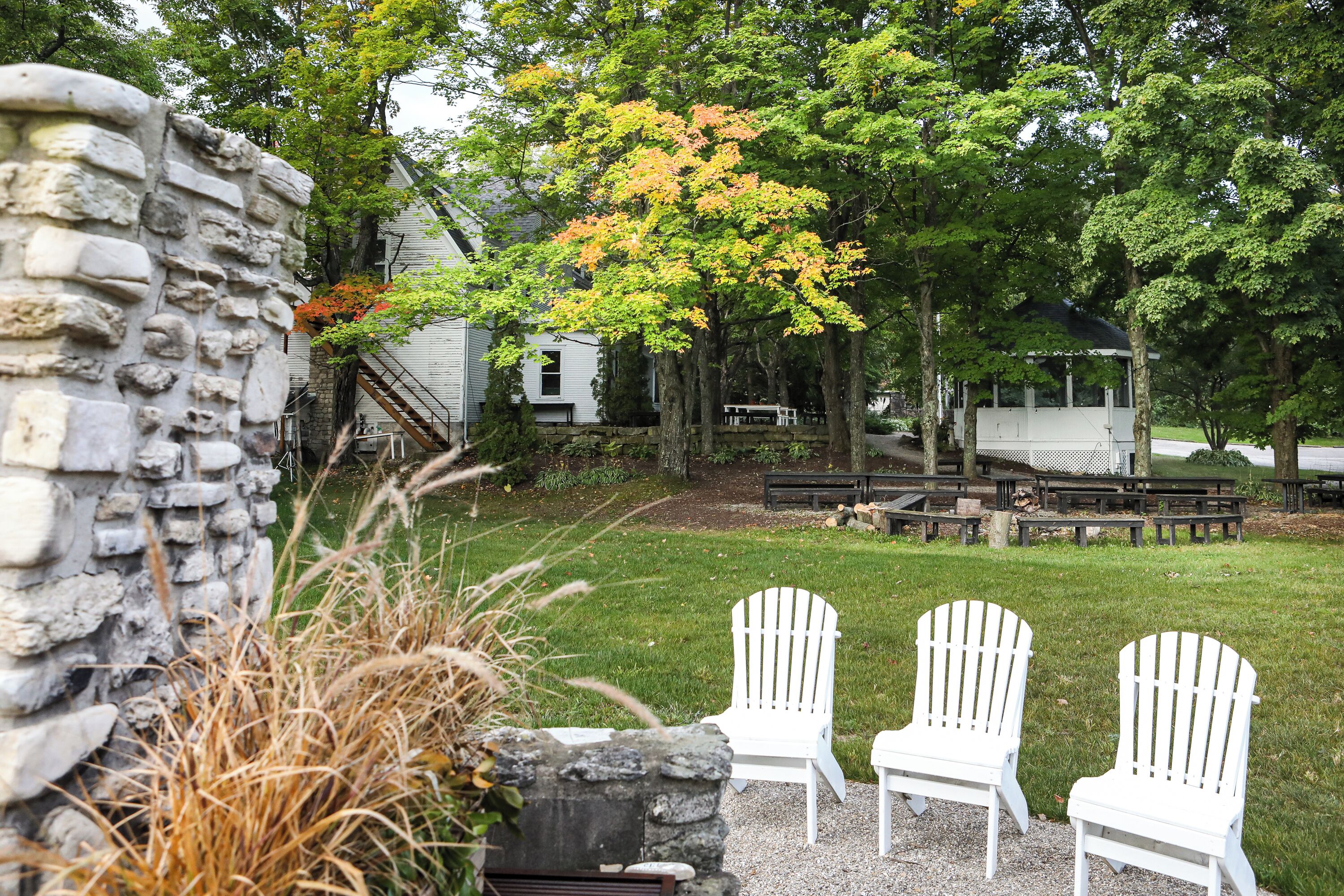 A stone wall, two Adirondack chairs, and a grassy area with trees and a wooden deck.