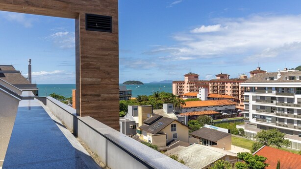A coastal residential area with a view of the sea, featuring modern buildings with balconies and a prominent wooden structure. - Penthouse 3 min From Jurere Beach - Mor0402 (Florianópolis)