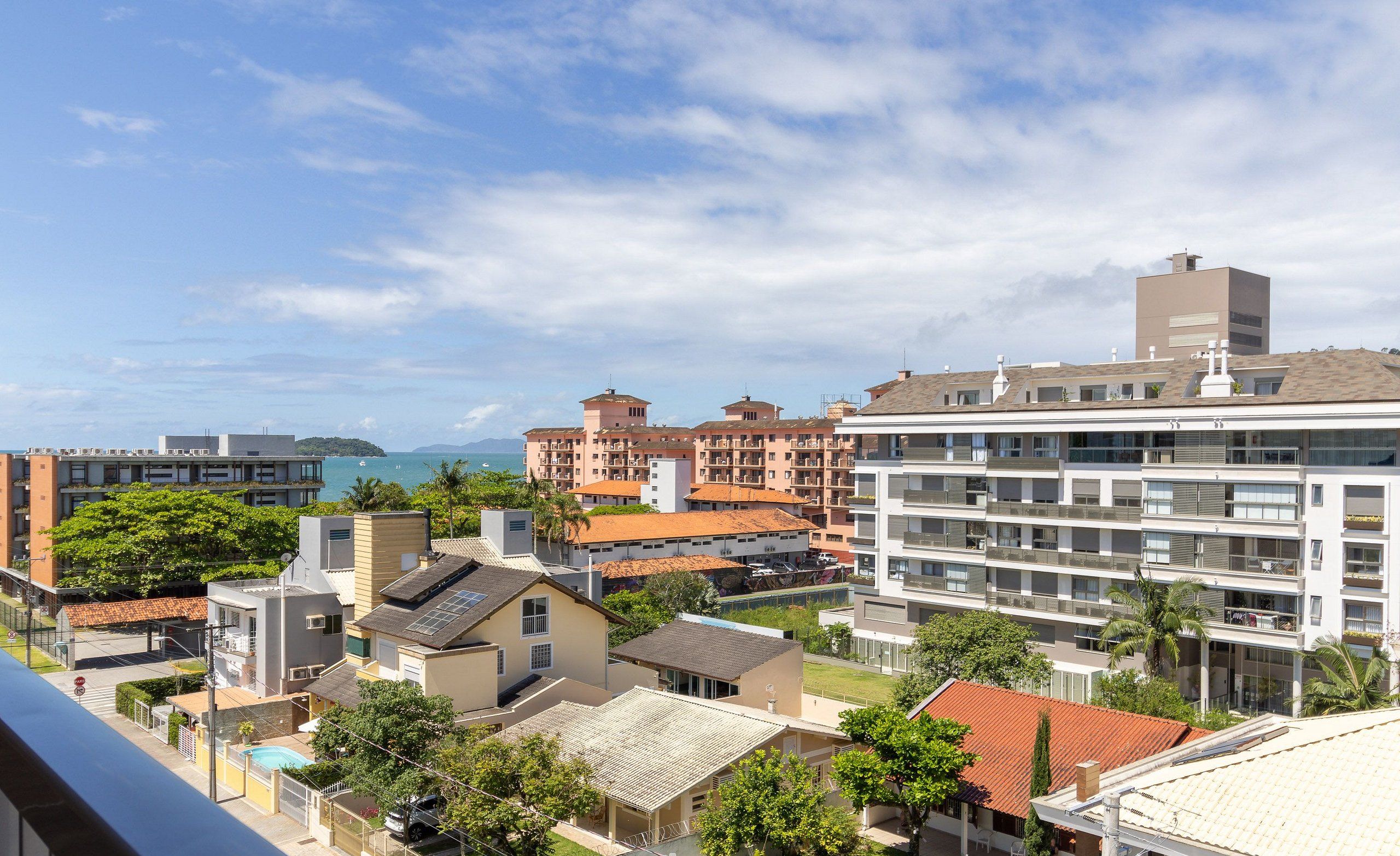 A coastal residential area with various buildings, including a large white apartment complex with multiple balconies and a smaller building with a red roof.