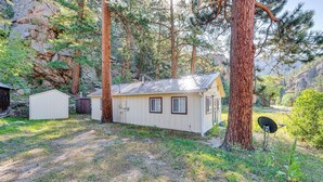 A small cabin with a metal roof, surrounded by tall pine trees and rocky terrain. - Hike, Fish & Relax: Cabin 4 Mi to Lake Estes! (Drake)