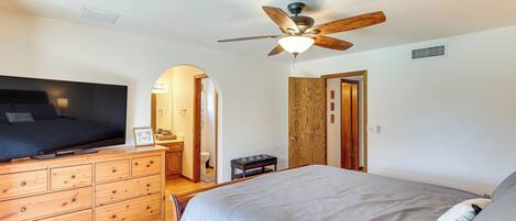 A bedroom with a bed, a wooden dresser, a ceiling fan, and a bathroom visible through an archway.