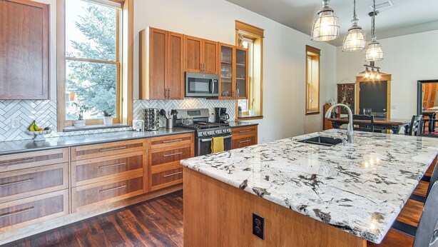A modern kitchen with wooden cabinets, a large island with a sink, a microwave, and a stove. There are pendant lights above the island.