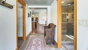 A hallway with a wooden bench, a rug, and a glass shower area.