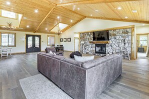 Un salon spacieux avec un grand canapé d’angle, une cheminée en pierre et un plancher en bois.