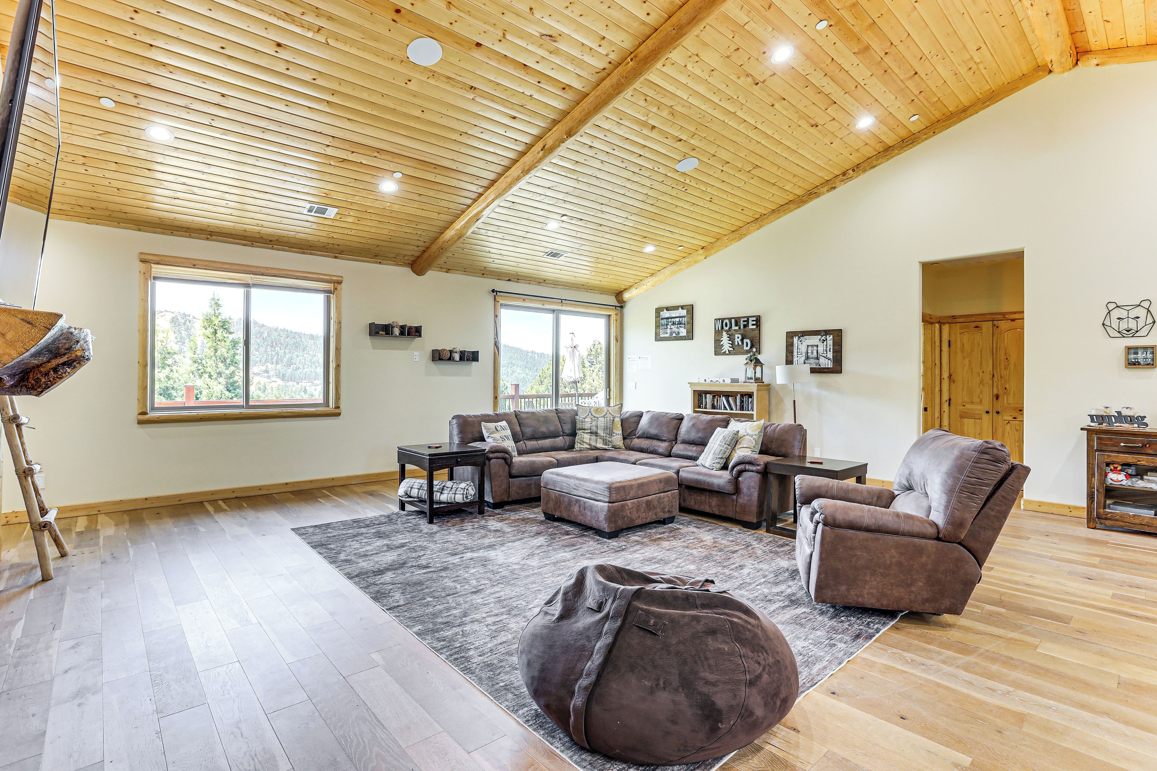 A spacious living room with a high wooden ceiling, large windows, a sectional sofa, a recliner, and a large bean bag.