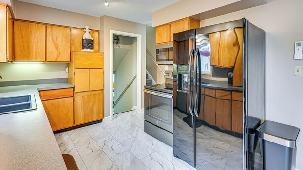 A modern kitchen with wooden cabinets, stainless steel appliances, and a marble floor. - 1 Mi to Dtwn: Suburban Home w/ Yard in Owosso (Owosso)