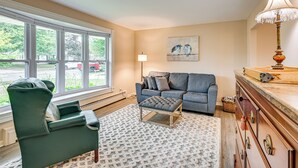 A living room with a green armchair, a gray sofa, a patterned rug, and a wooden cabinet. - 1 Mi to Dtwn: Suburban Home w/ Yard in Owosso (Owosso)