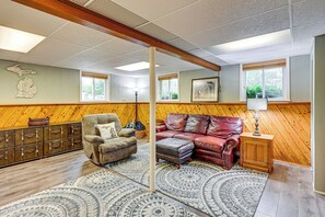 A room with a wooden floor, a patterned rug, a leather sofa, a wooden cabinet, and a map on the wall. - 1 Mi to Dtwn: Suburban Home w/ Yard in Owosso (Owosso)